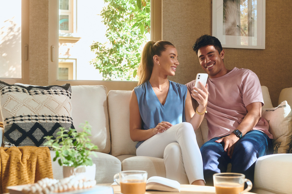 Couple using Irvine Company apartment living apps on smartphone in a stylish, well-lit living room.